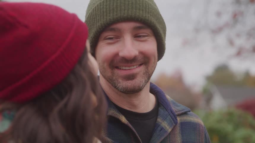 The video shows a man and woman in winter hats standing sidebyside they are both smiling and looking at something or someone just out of frame