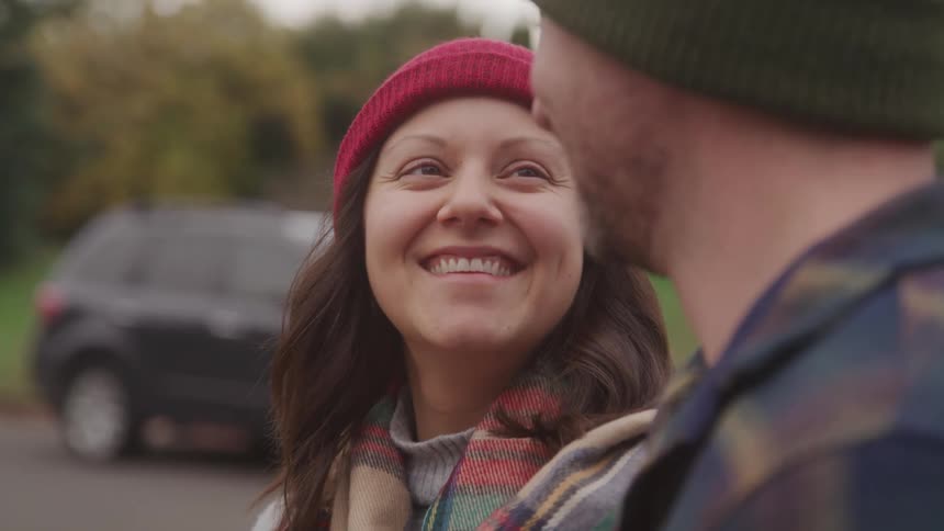 A woman in a red beanie smiles warmly at a man during a walk on a chilly day