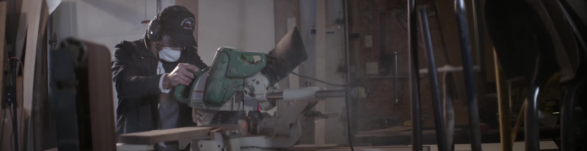 A man wearing a mask saws a piece of wood