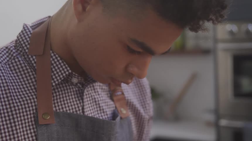 Man wearing an apron and checkered shirt looks focused while cooking