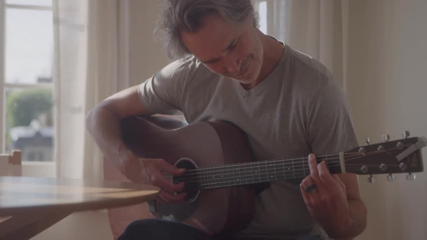 A man smiles as he plays the guitar