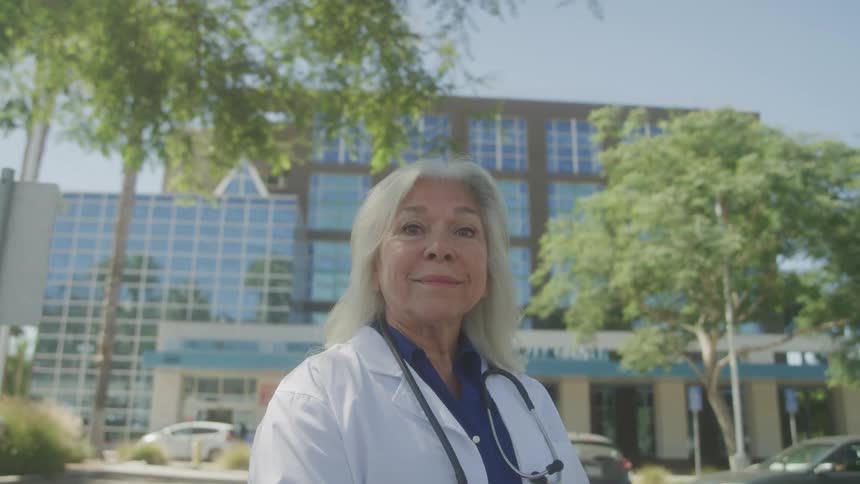 Smiling female doctor stands outside hospital