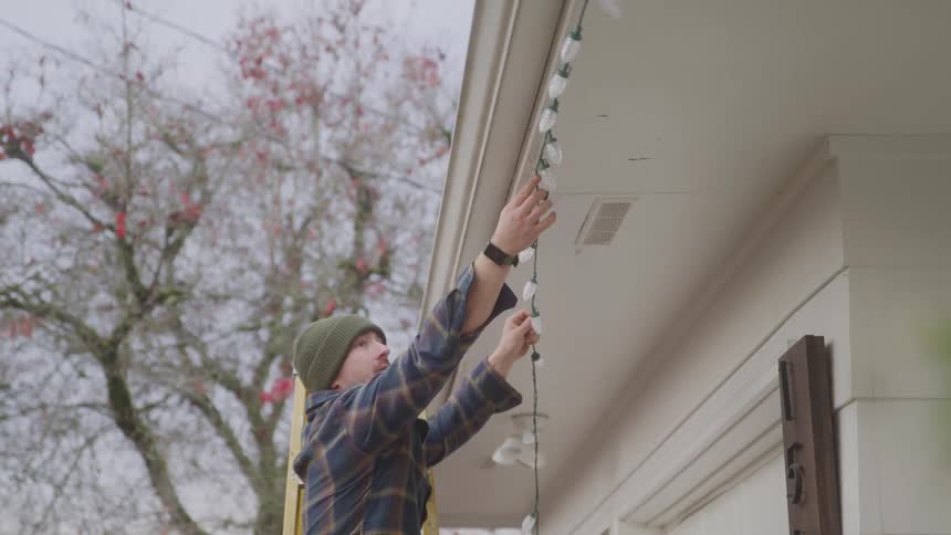 The man climbs the ladder and hangs christmas lights