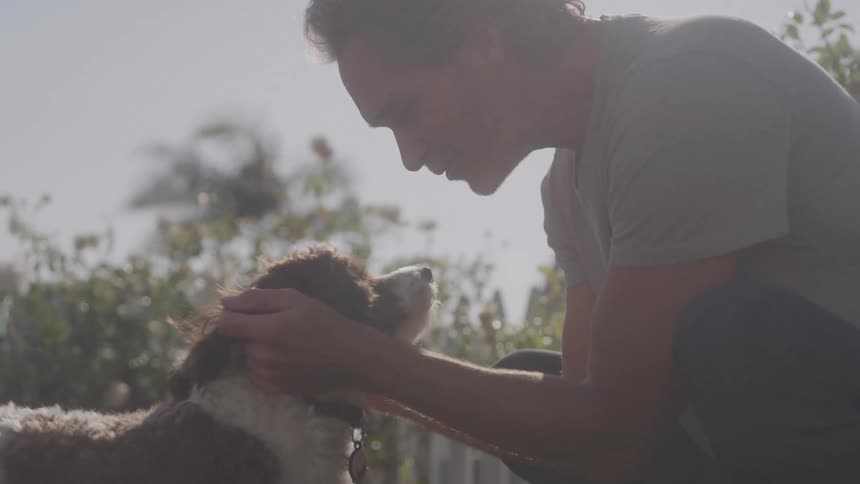 A middleaged man pets his dog on the lawn at midday