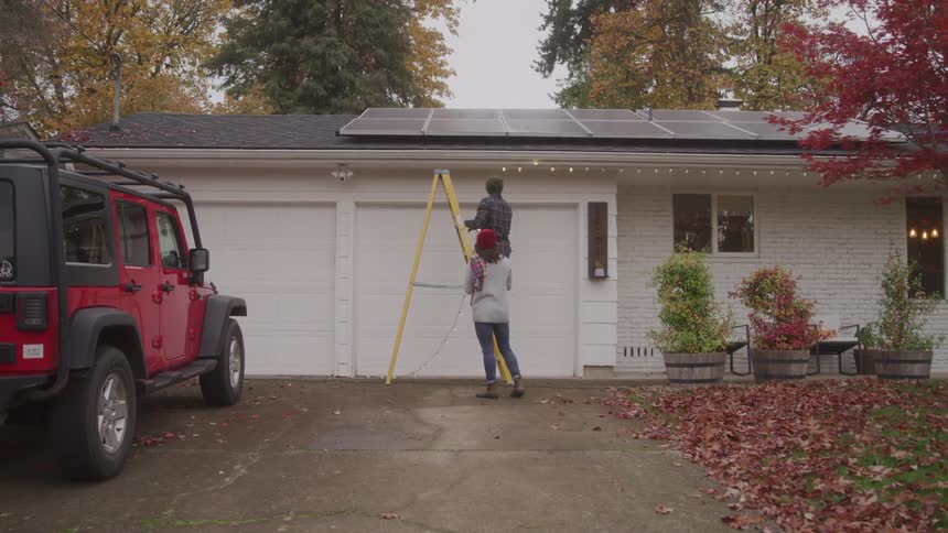 A young couple install festive lights around their building outdoors during daytime