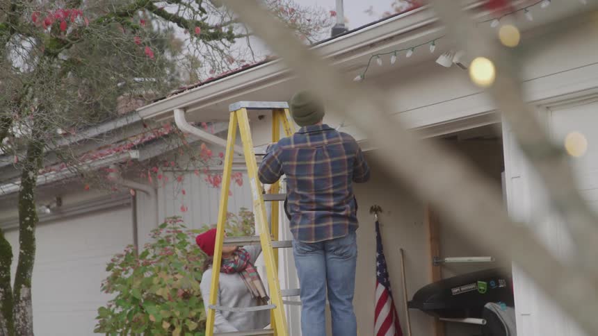 Two people decorating a houses garage with christmas lights