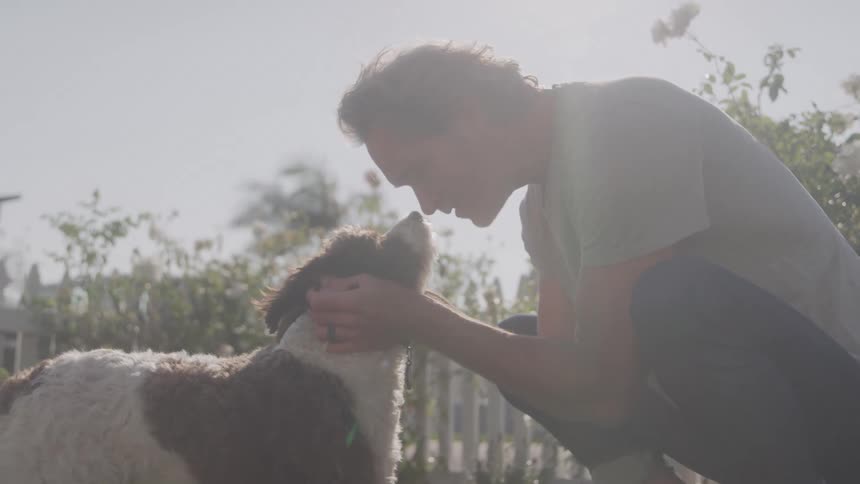 Man crouches down touching his face to the dog while petting it in the garden