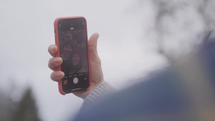 Hand holds a phone showing a selfie of a smiling couple wearing winter hats