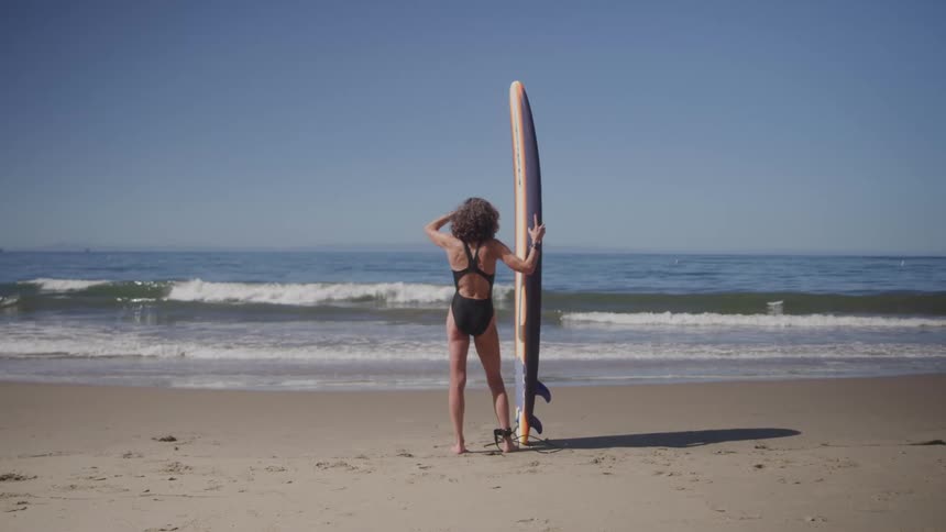 A woman is holding a surfboard on the beach