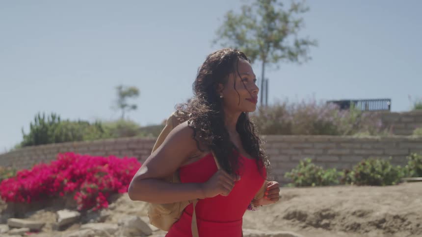 Woman in a red dress walks outdoors carrying a backpack