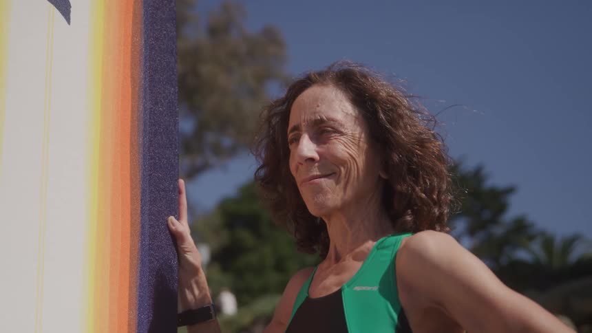 Woman in a green swimsuit holds a surfboard outdoors under a blue sky