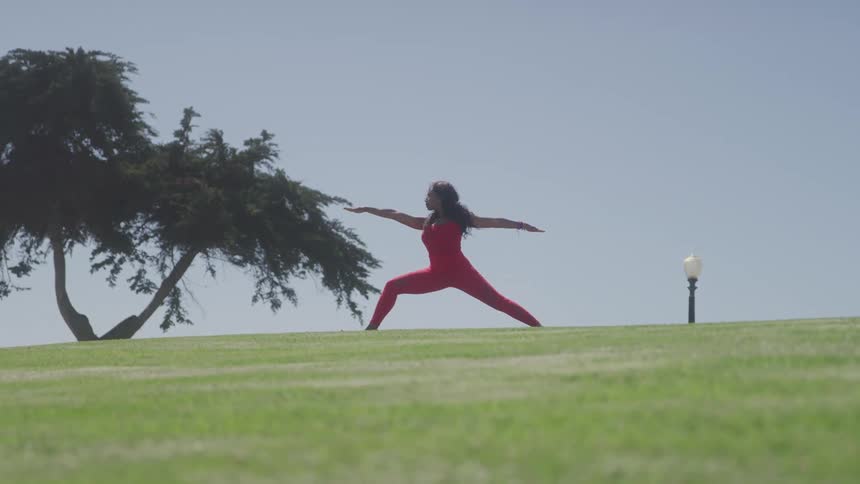 Woman in red outfit practices yoga in warrior pose on an open field