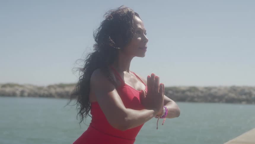 Woman in a red dress practices a meditation pose by the sea