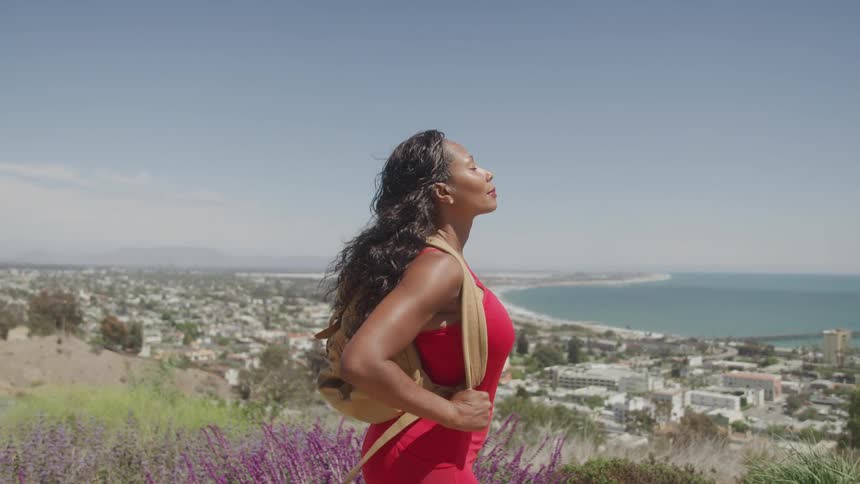 A woman stands on a scenic overlook taking in a breathtaking view of the ocean and a coastal city below her