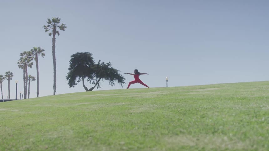 A woman in athletic wear stretches on a grassy hill under a clear sky