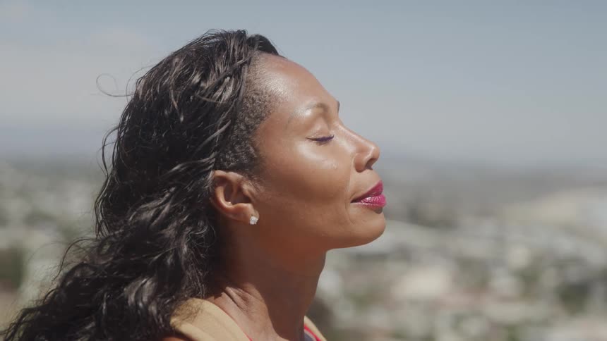Woman with closed eyes takes a deep breath under the sunlight