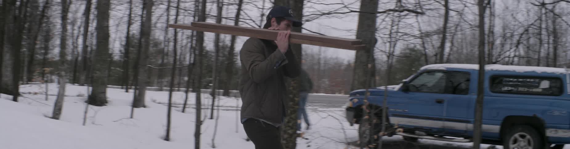 A man carries some boards over to a house