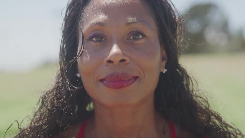 A woman with long black hair and red lipstick stands under the sun