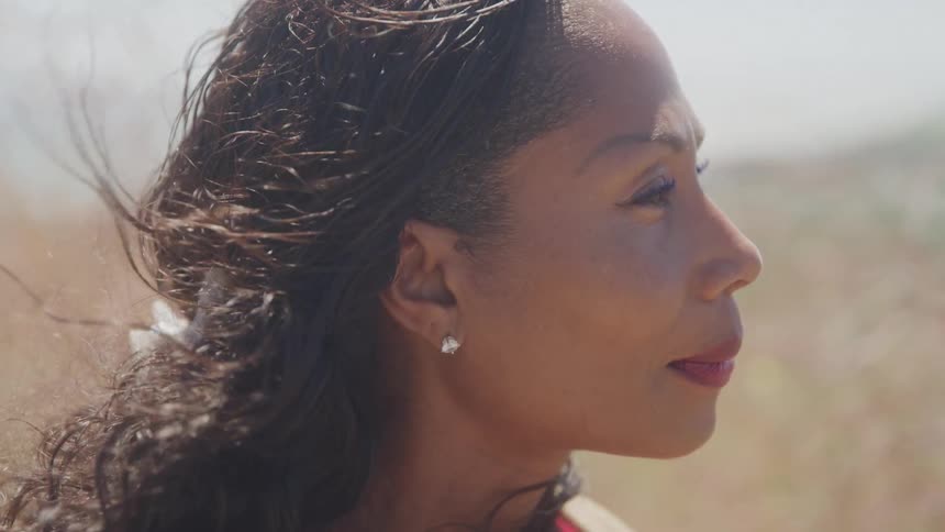 The video shows a closeup of a womans face with her curly hair blowing in the wind she is smiling and looking off to her right