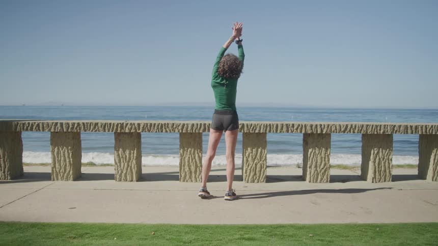 The woman is stretching by the beach on a sunny day