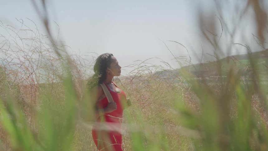 A woman in a red dress is standing in tall dry grass