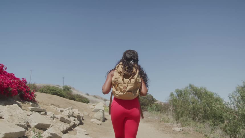 A young black woman walks up a rocky terrain outdoors during daytime
