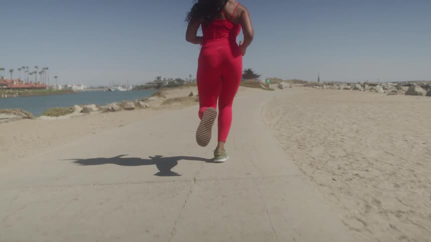 Woman in a red sports jumpsuit runs on a seaside trail