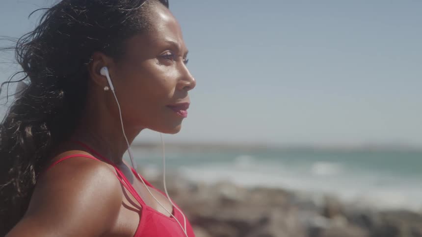 Woman in red sportswear with earphones looks at the sea