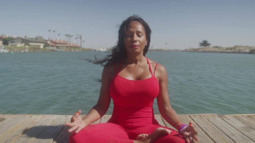 The woman is meditating by the water on a windy day
