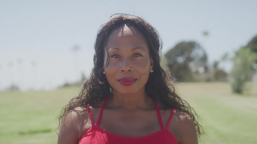 A woman wearing a red dress and red lipstick stands out in a sunlit field at midday