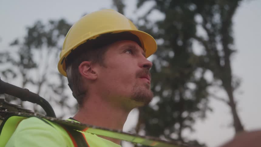 The worker is holding a chainsaw