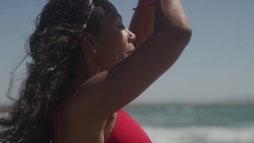 Woman in a red dress practices a meditation pose by the sea