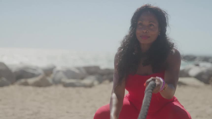 A woman exercises with battle ropes on a sunny beach