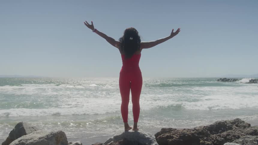 A woman in pink outfit is doing yoga on the rocky beach