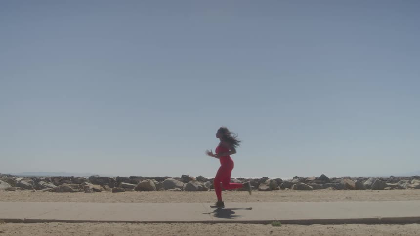 Woman in a red sports jumpsuit runs on a seaside sidewalk