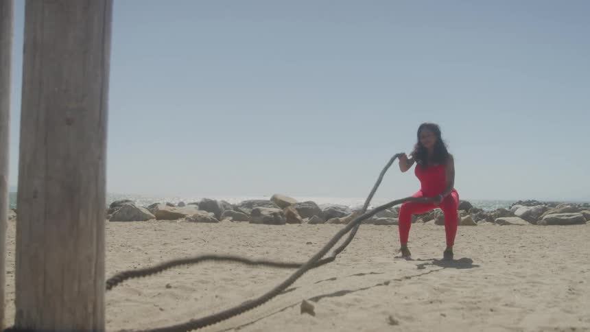 Woman exercising with ropes on the sand of a sunny beach