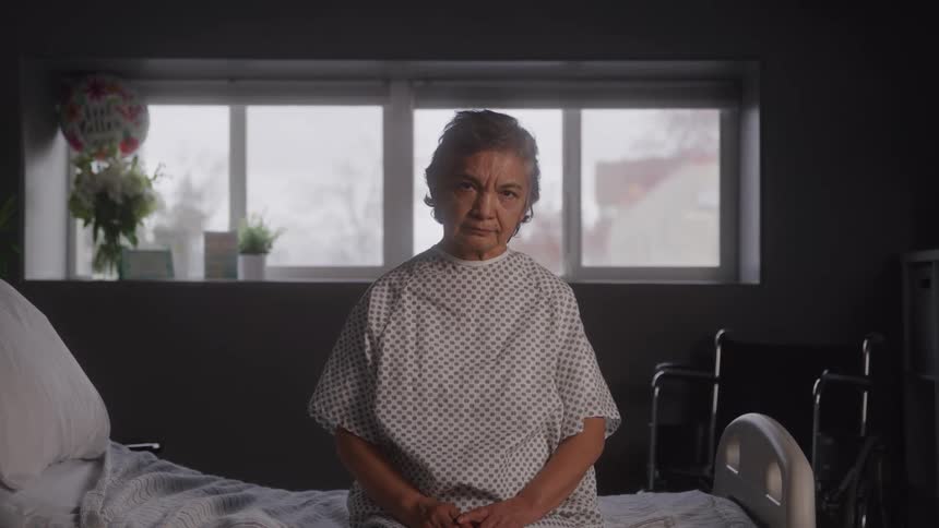 The woman is sitting on the hospital bed