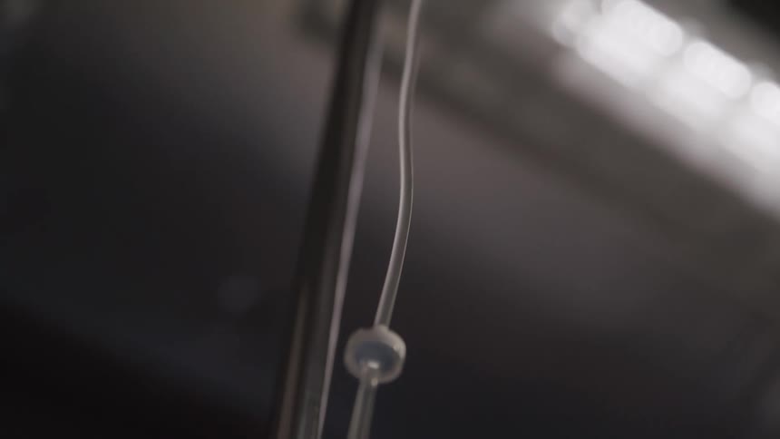 A hospital iv bag hangs from a metal pole in a dimly lit clinical setting