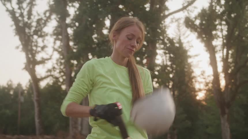 Woman wearing a white helmet and green shirt works with a shovel outdoors at sunset