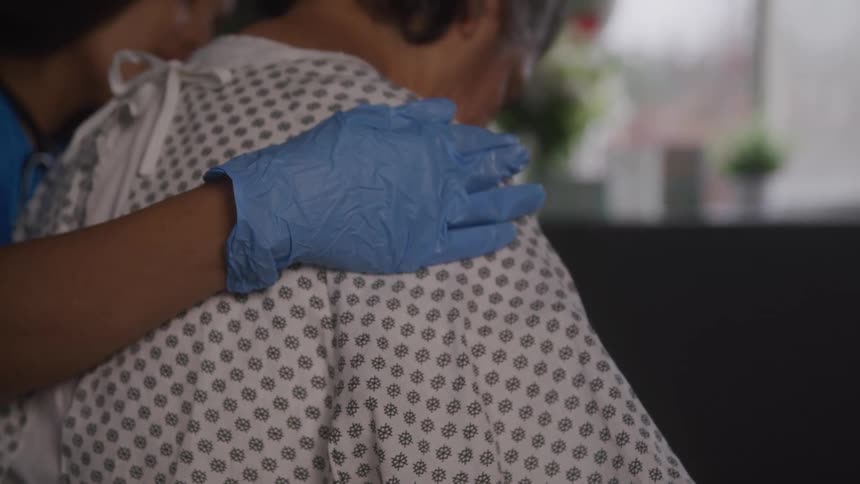 Nurse comforts a patient while sitting next to them in the hospital room