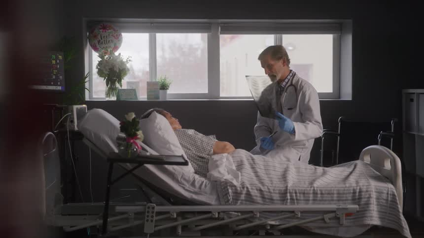 Doctor shows an exam to a patient lying in a hospital bed