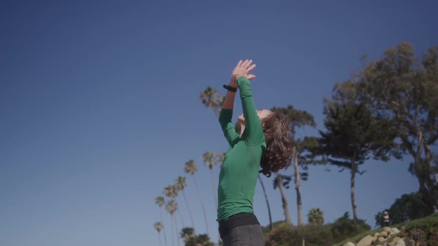 Person in a green shirt stretches arms on a sunny beach