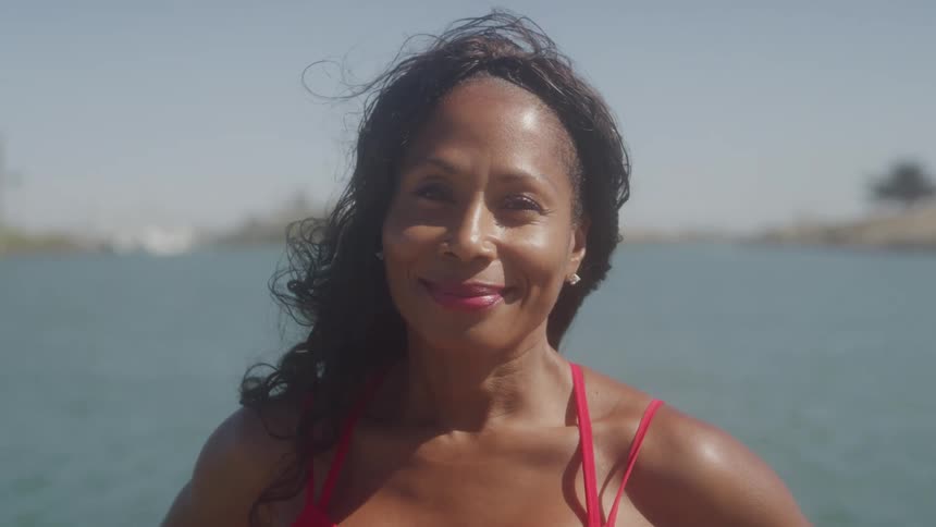 Woman in a red dress smiles in front of the sunny sea