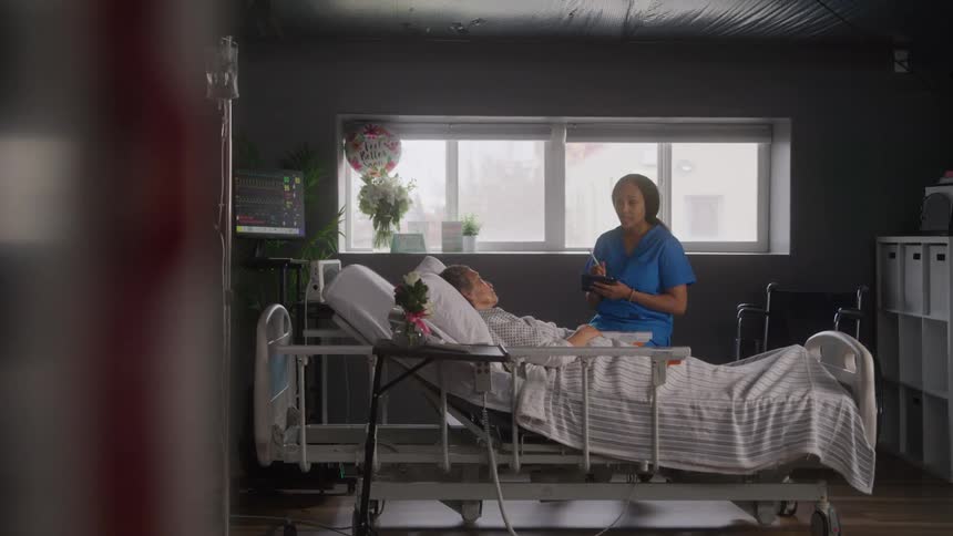 Nurse in blue scrubs attends to a patient lying in a hospital bed