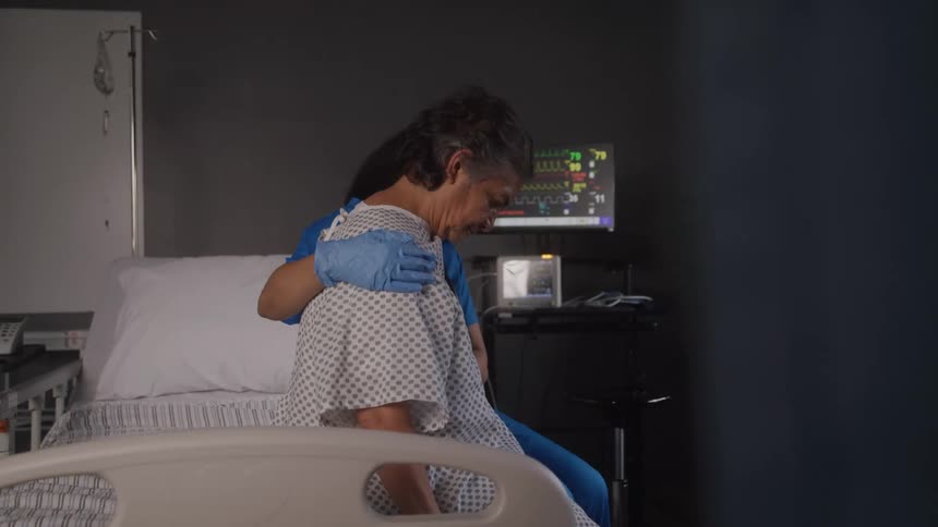A patient sits on a hospital bed while a nurse seated beside her attends to her
