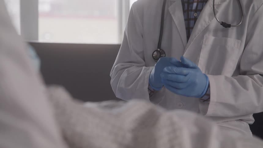 Doctor with a stethoscope adjusts blue gloves while attending to a patient