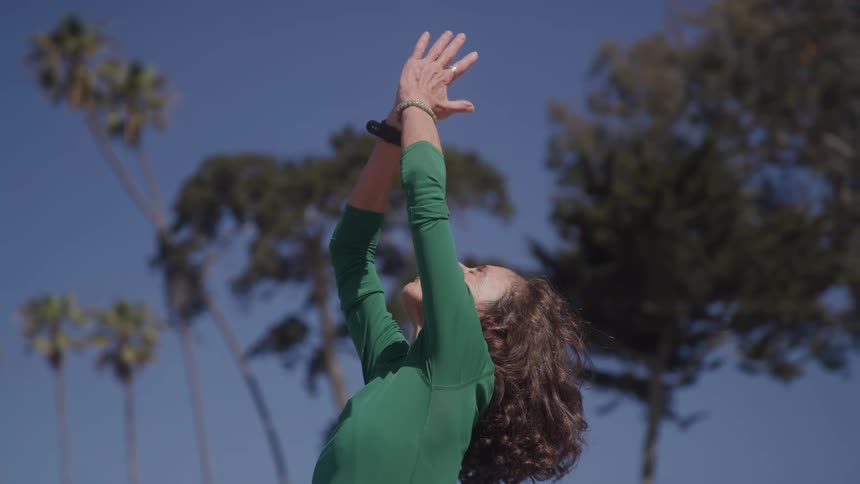 Woman with a serene expression raises her hands in a contemplative gesture under a blue sky