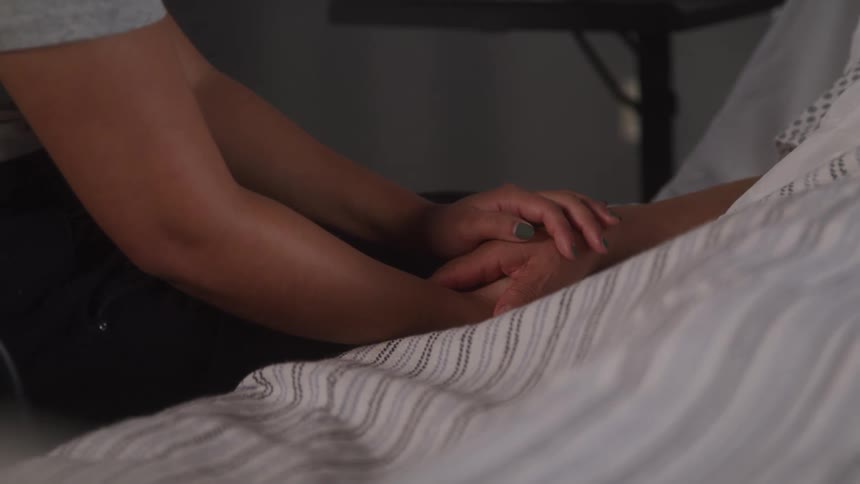 A hospital visitor is holding hands with a patient