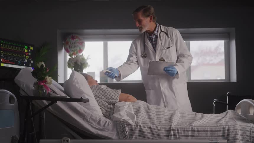 A patient lies on a hospital bed being checked by a doctor at midday as the doctor talks to the patient during the examination