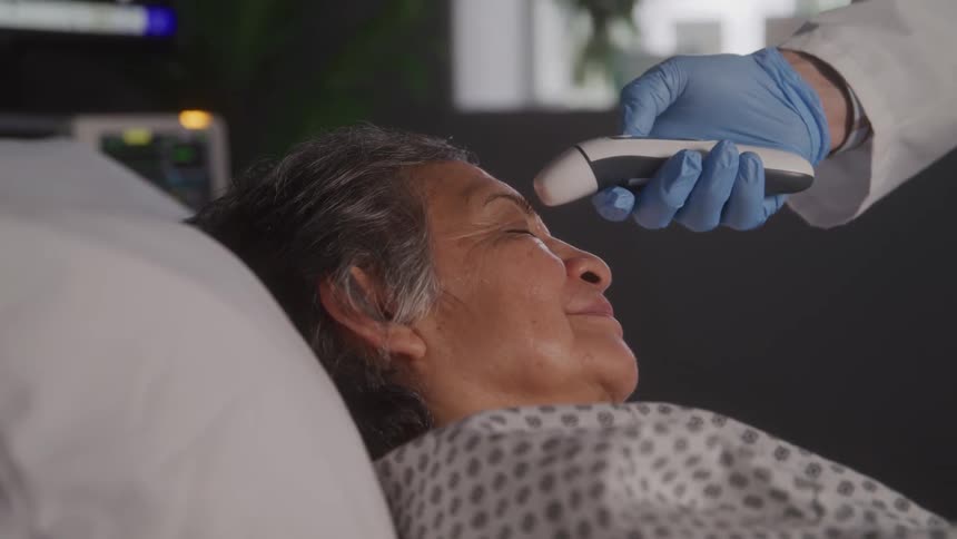 Woman lying in a hospital bed has her temperature checked with a digital thermometer